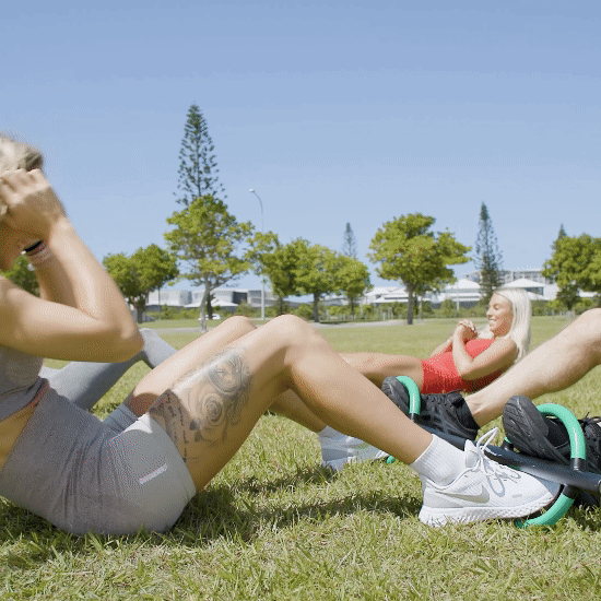 GIF Image of 3 women and a man interlocking their feet into the handles of the Butterfly Barbell to enable them to do sit-ups.